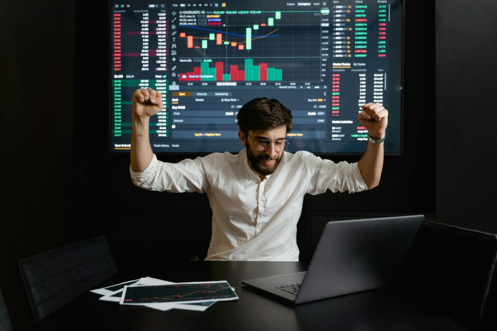 Successful stock trading investor celebrating gains while analyzing live market charts and trading data on multiple screens